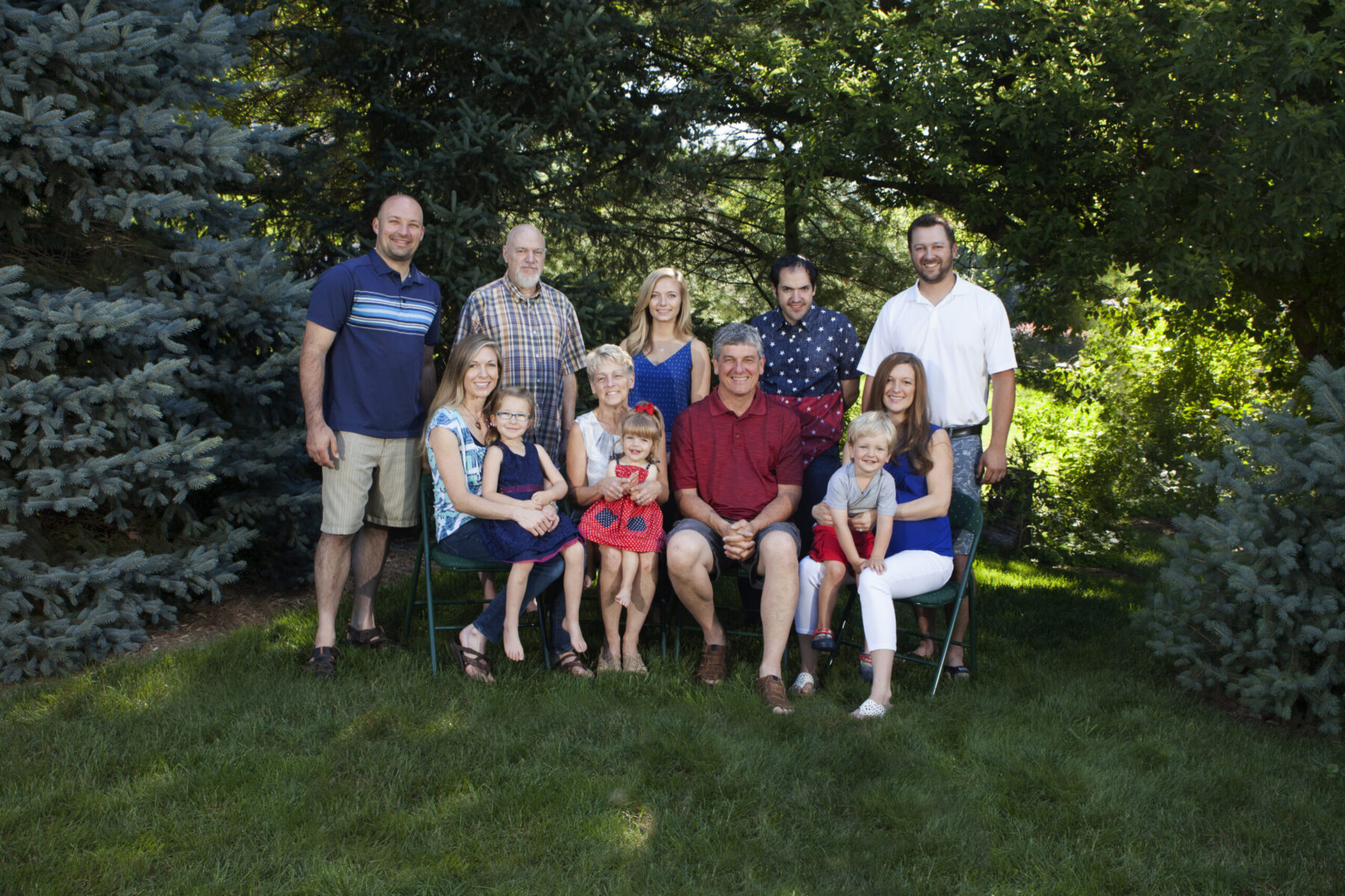 A three-generation family poses together for an outdoor portrait in a garden setting.