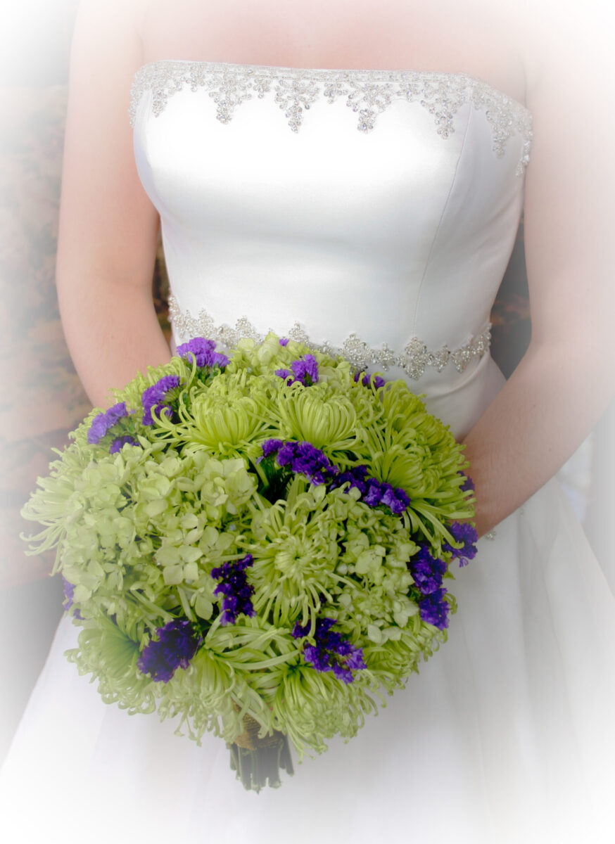 Bride holding a bouquet of green and purple flowers.